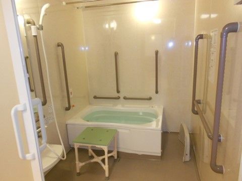 壁に縦向きと横向きの多くの手すりが設置された浴室。バスタブの横には、緊急時用のナースコールが備え付けられている。