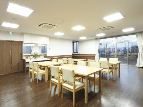 大きな窓に白いカーテンが掛けられ、外の庭が見える。部屋の中心に数組のダイニングテーブルと椅子が配置されている。