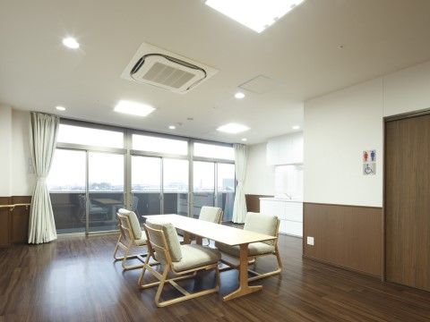 部屋の中央にナチュラル色の木材の長いテーブルが置かれている。テーブルの周りに白色とナチュラル色の木材の４脚の椅子が配置されている。