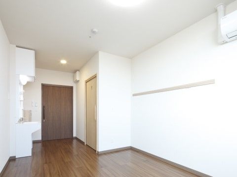 白いクロスの壁にフローリングの床のシンプルな部屋である。スライドドアの入り口を入ると洗面台が設置されている。