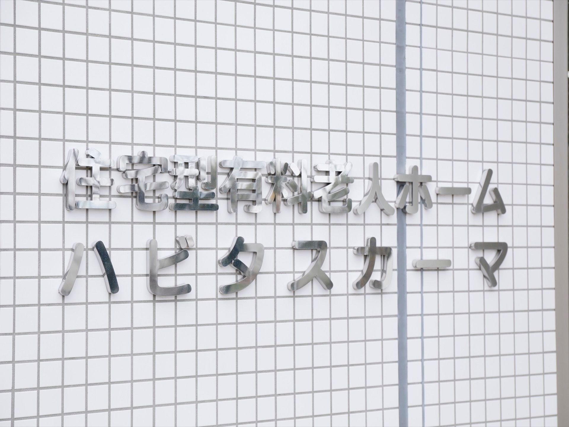 施設名を外壁に表示している。グレーの壁にシルバーで書かれている。大きな文字でわかりやすく書いている。