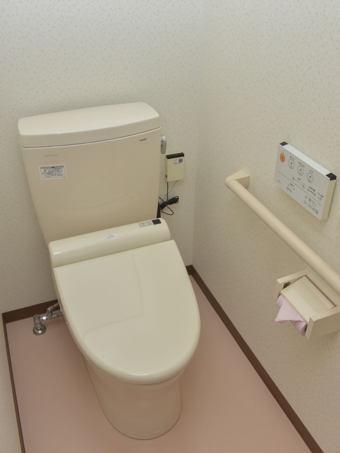 ウォッシュレット付きの温水トイレ。壁面に手すりがついている。トイレットペーパーの端はきれいに三角に折られている。