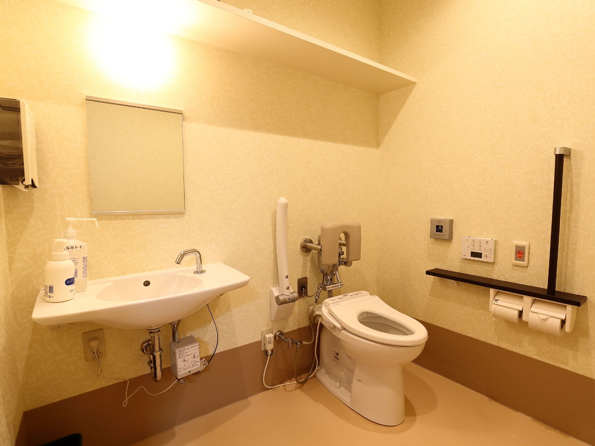 トイレの個室は広々としていて洗面台が併設されている。便器にはもたれかかれる背もたれがあり、可動式の手すりがついている。