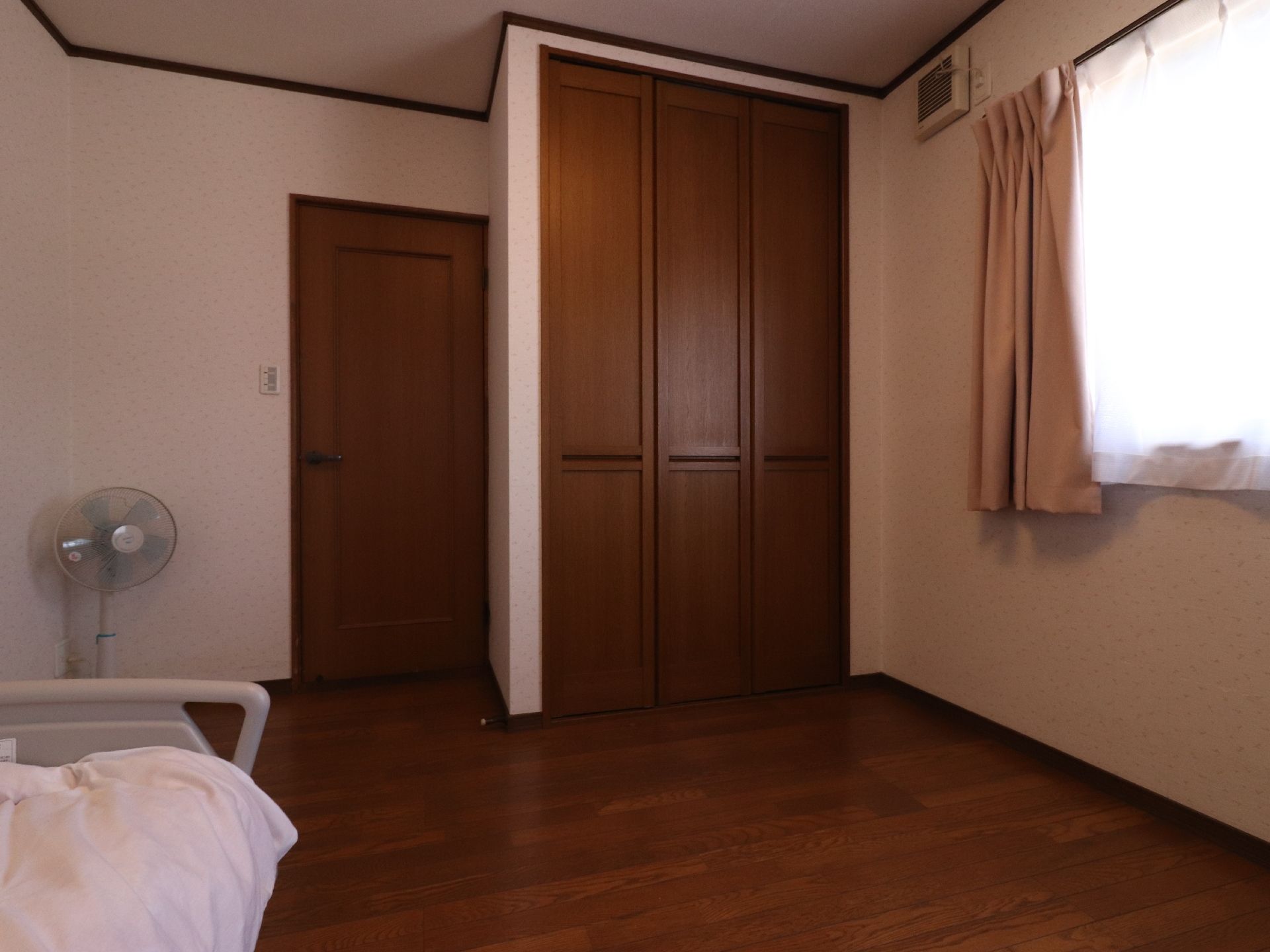 焦げ茶色と白色仕様の居室である。ドアから少し進んだ左側に収納庫が設置してある。角には扇風機が置いてある。