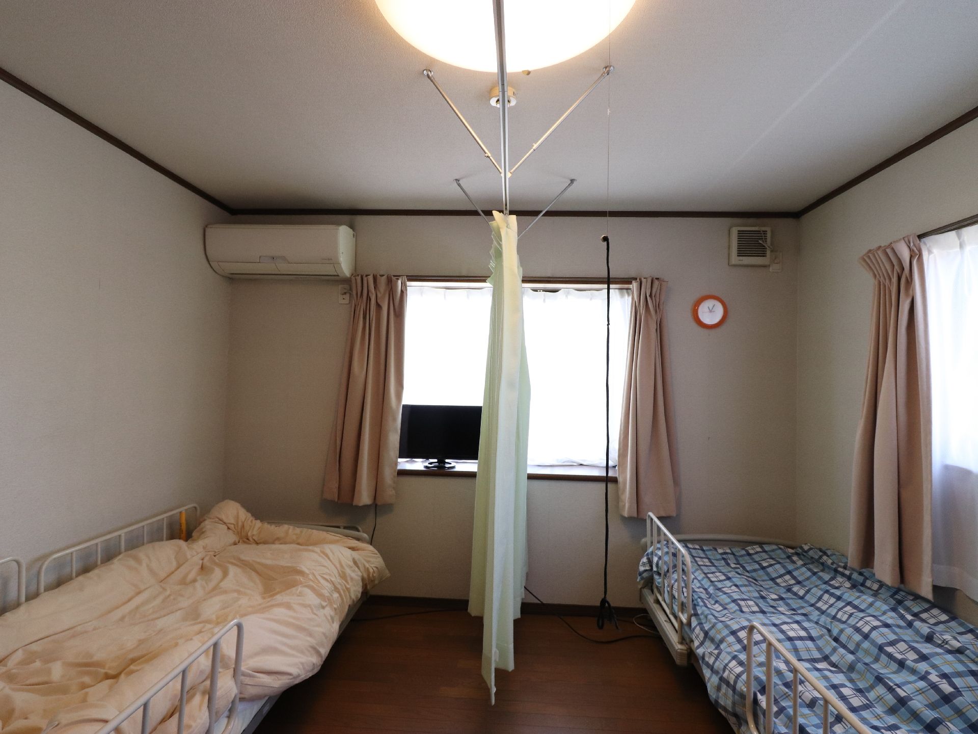 正面と横側に窓がある。天井にはエアコンが設置され、窓の前の台の上にテレビが置かれている。壁には時計が掛けてある。