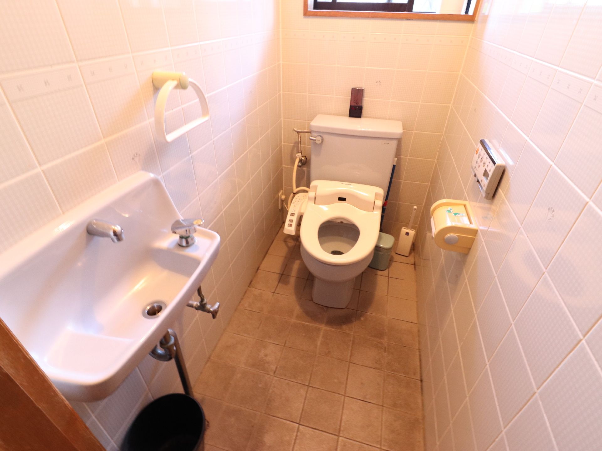 トイレの床や壁はタイル張りになっている。奥には洋式トイレが設置され、手前には手洗いが取り付けられている。