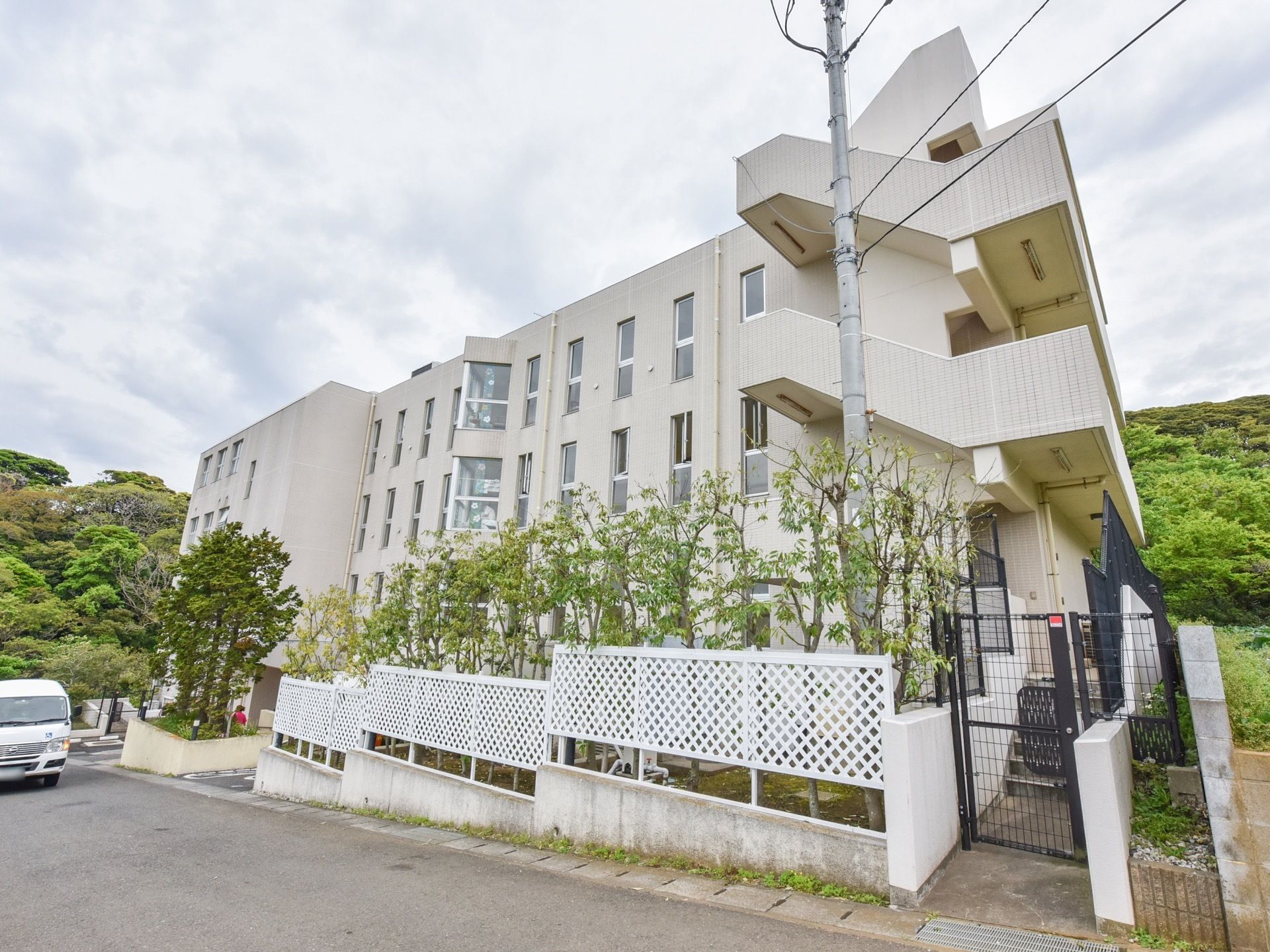非常階段が設置されたホーム。道路に面して木が植えてあり、白い柵が立てられている。施設前にワゴン車が停められている。