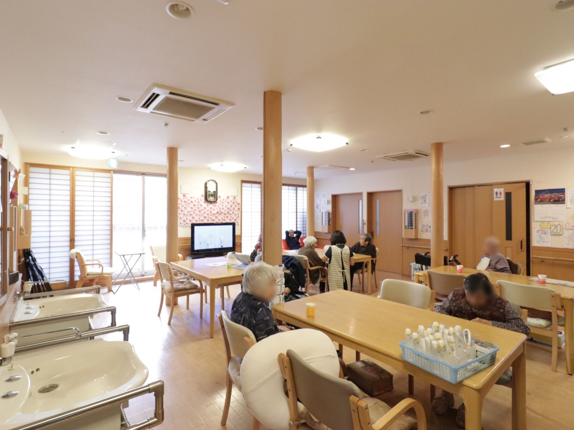 リビングには、４人掛けのダイニングテーブルが配置されている。左右に手すりが備わった洗面台が２台左の壁に設置されている。