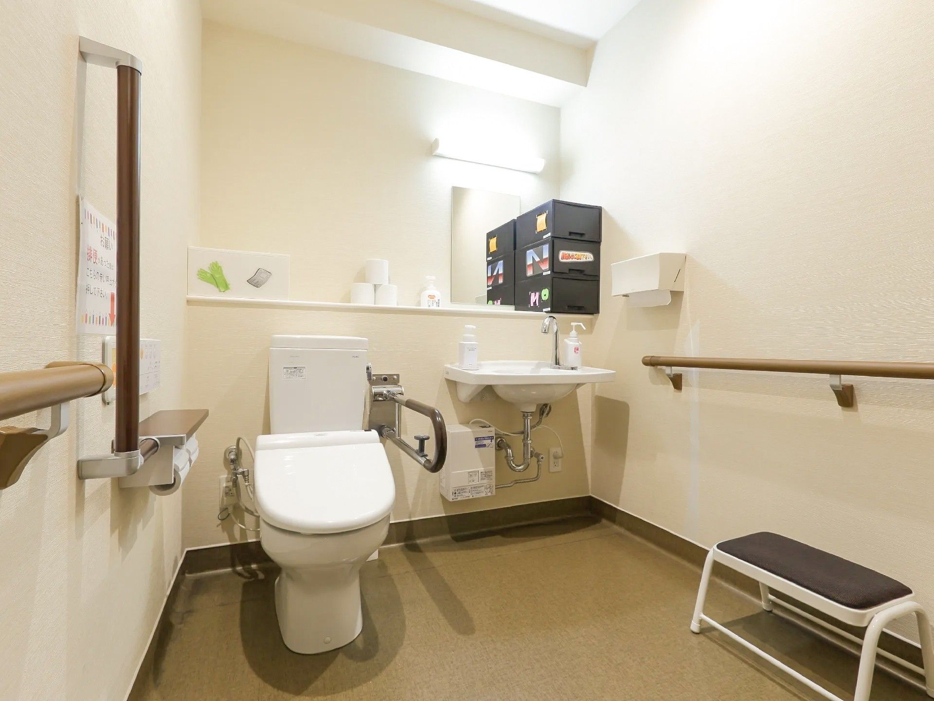 温水洗浄便座付きの洋式トイレが設置されている。壁には手すりやナースコールが付いている。隣には鏡の付いた洗面台が置かれている。