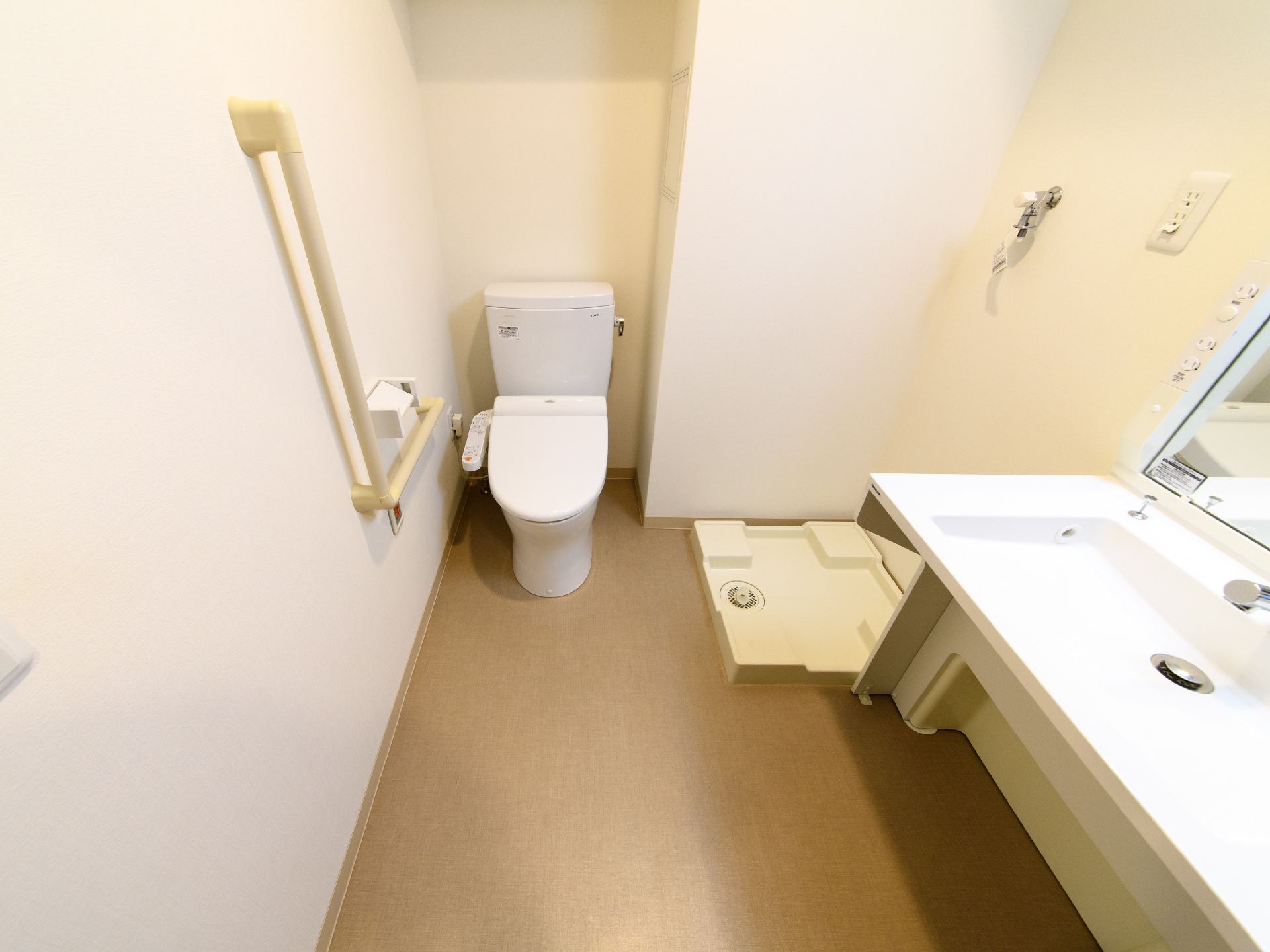 トイレは温水洗浄便座付きである。左側の壁には手すりとナースコールが設置されている。右側には洗濯機置き場が設けられている。