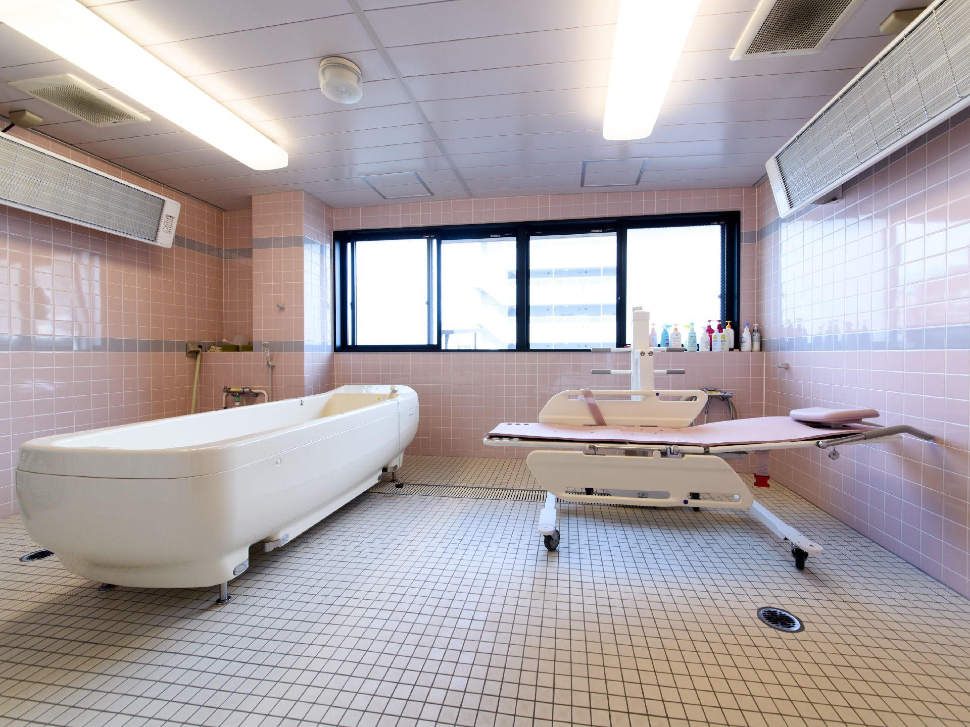 浴室の壁は淡いピンク色のタイル張りで、窓の高さにグレーのボーダーが描かれている。床はフラットなタイル敷きである。