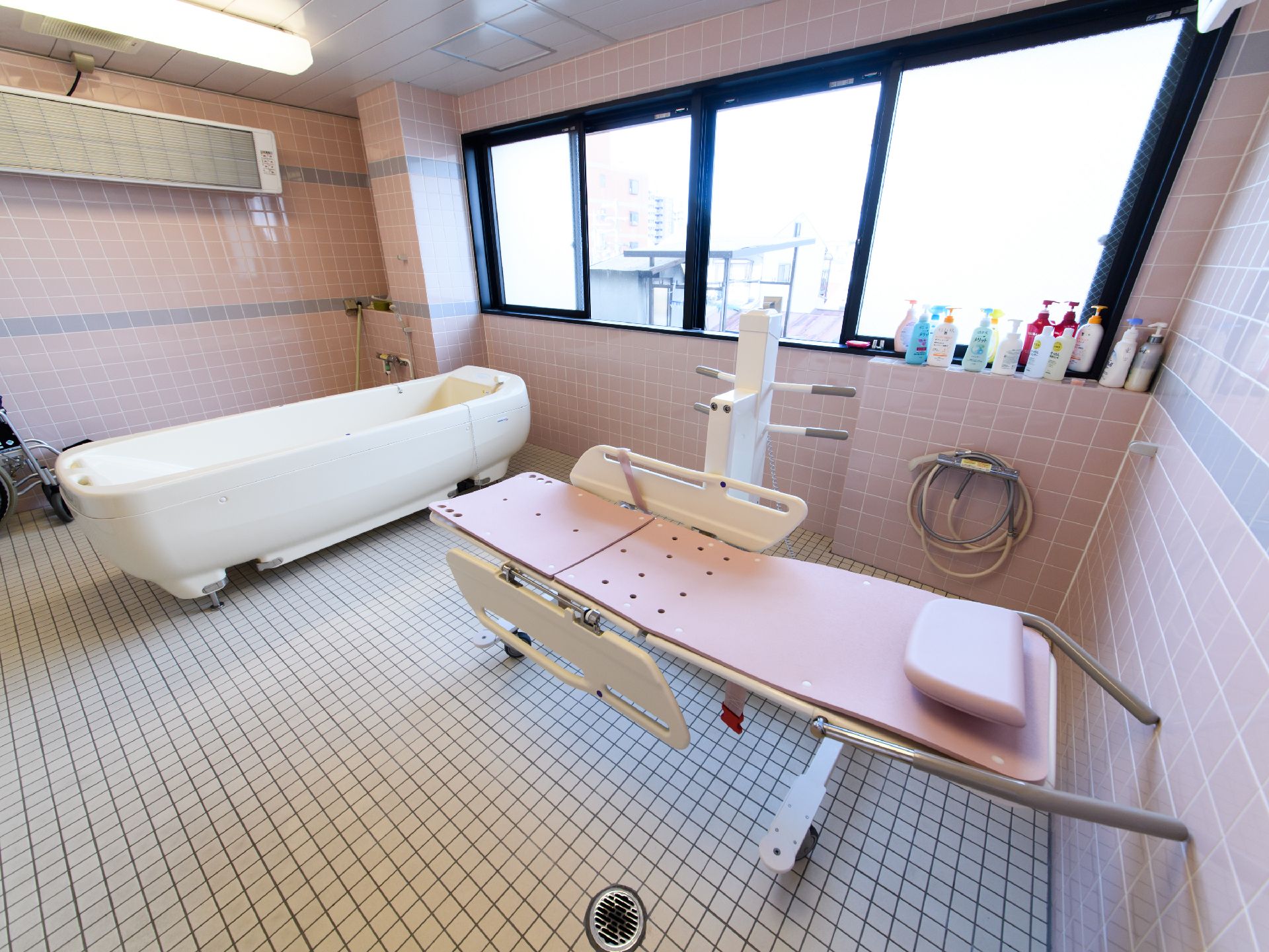 浴室の床はフラットなタイル敷きで、入浴用のストレッチャーが安全に移動できる広さが確保されている。壁に窓が設けられている。