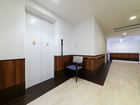 エレベーター前の床はブラウン系の2色でデザインされている。入り口ドアの色は白で、右側の壁には操作パネルがある。