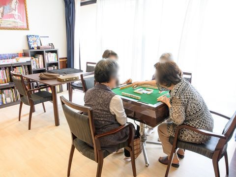 娯楽スペースには大きな窓があり、日差しを調節するカーテンが掛けられている。4人の入居者様が麻雀を楽しんでいる。