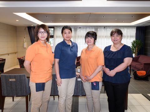 テーブルセットの前に立つ、紺色とオレンジ色の服を着た4人の女性職員