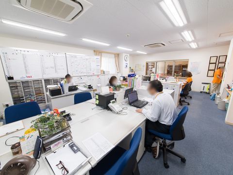 デスクが向かい合う形で配置された、明るい照明の事務室
