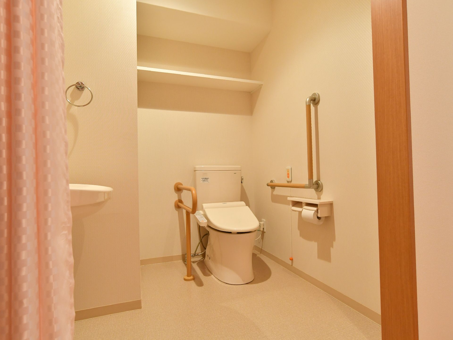 手前にはカーテンが付いている。奥には便器があり、近くには手すりが付いている。右壁には緊急用の装置が設置されている。