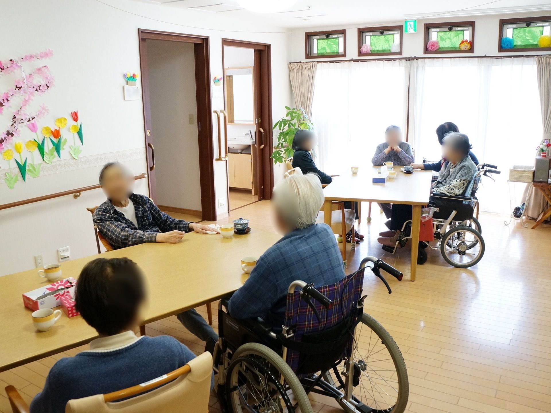 各居室前のオープンスペースにはダイニングテーブルが配置され、入居者様がテーブルを囲んでおしゃべりをしている。