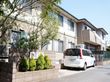 施設の建物は２階建てで、側面の外観は各居室のガラス窓が並び日が当たっている。敷地と道路の境界線上には、石造りの塀があり、木が植えられている。