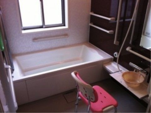 窓の付いた明るい雰囲気の個人用ユニットバスの様子。安全にご利用いただけるよう、手すり、呼出ボタン、シャワーチェアが備わっている。