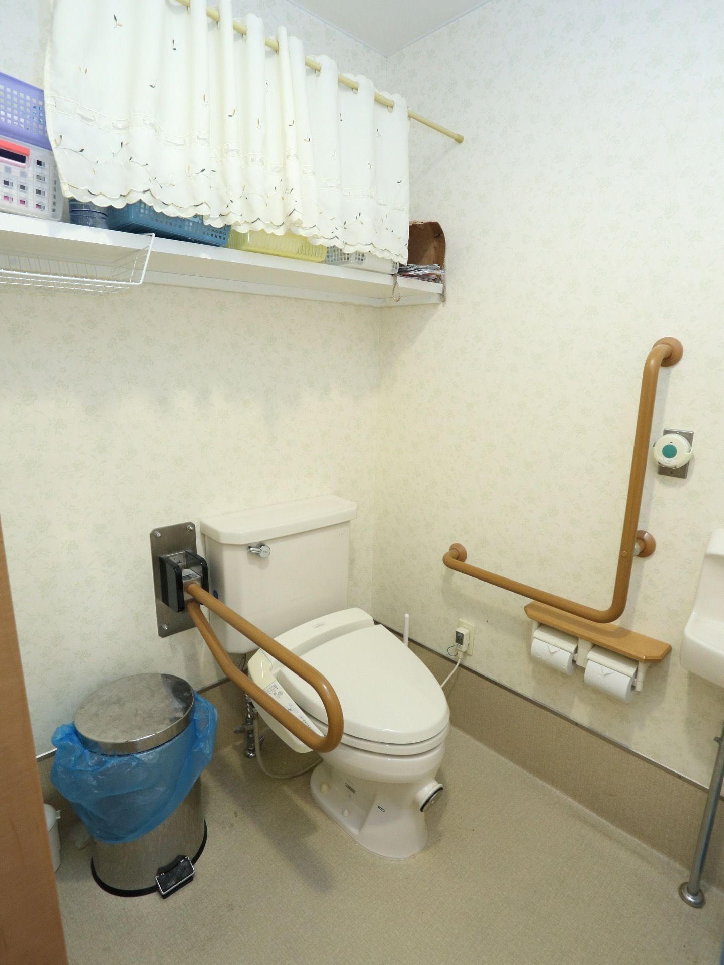 清潔で広いスペースに、便器と手洗い器が設置されている。後方の壁には大きな棚があり、沢山の物が保管できる。