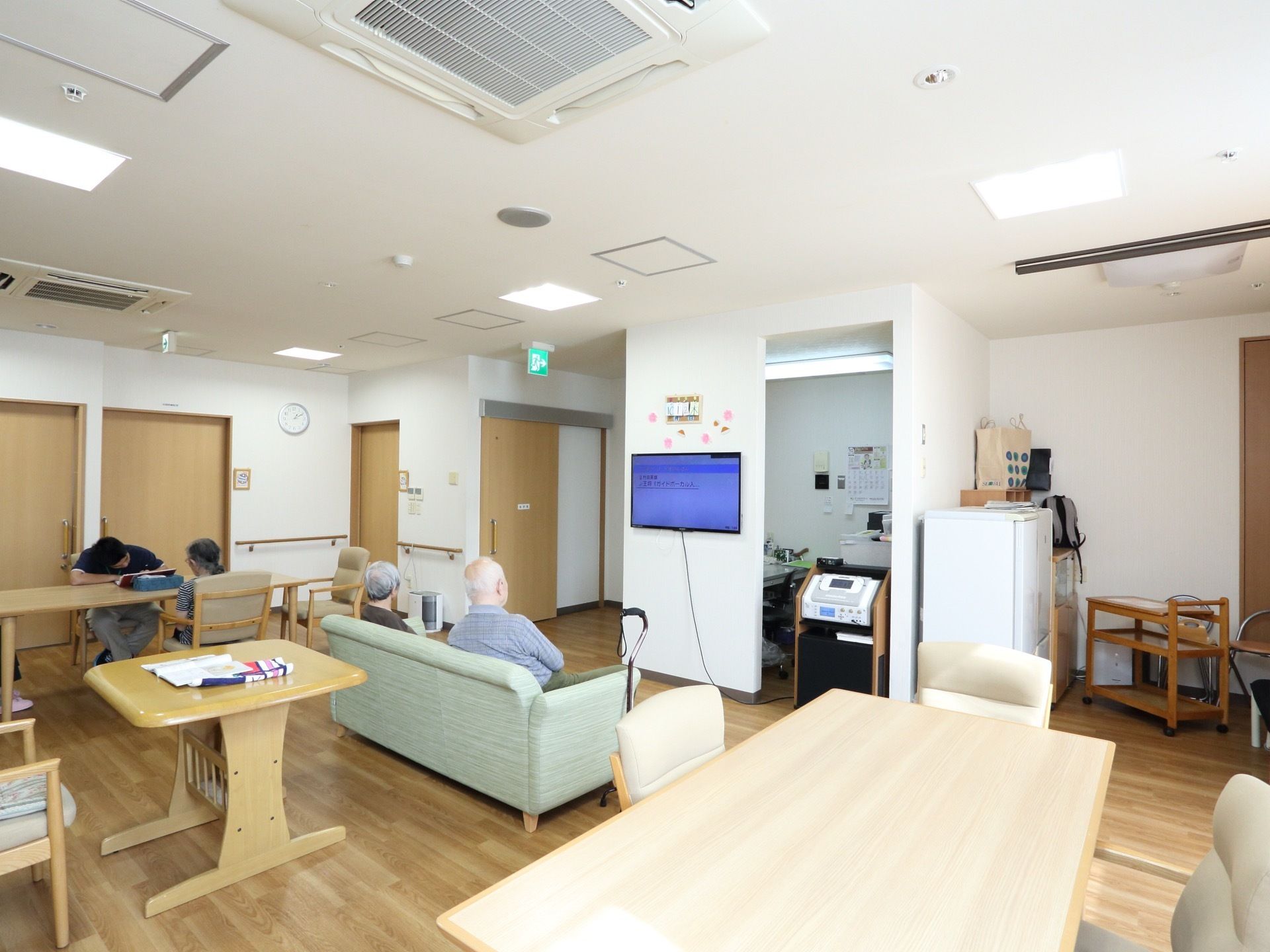 明るいスペースに、大小さまざまなテーブルと、椅子、ソファが置かれている。壁には薄型のテレビが掛けられている。