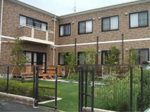 施設の建物の横に、芝生や木々が植えられている広い庭