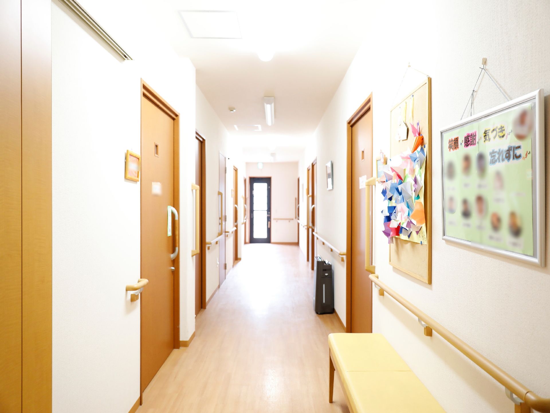 白い天井と壁で明るい廊下になっている。木目調のドアと床で落ち着いた雰囲気になっている。手すりが壁に設置されていて、安全に移動できる。