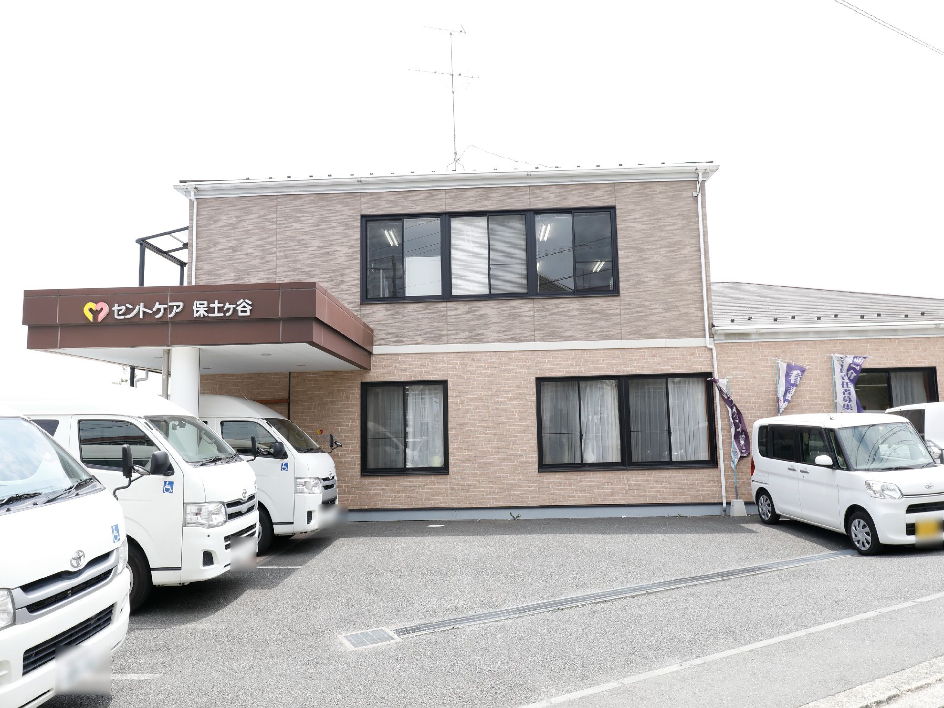 施設の建物は2階建てで、外壁が優しい雰囲気の薄いピンク色になっている。建物前には広々としたスペースがあり、駐車場が広くとられている。