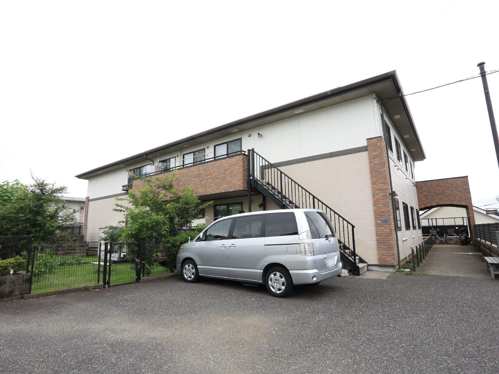 建物は2階建てで、薄いピンク色の外壁になっており茶色のレンガがアクセントになっている。外側に階段があり、いざという時に安心。