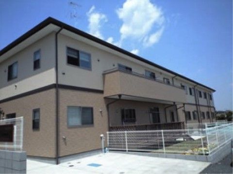 二階建ての温かみのある外観の建物と白いフェンスで囲われた専用の庭