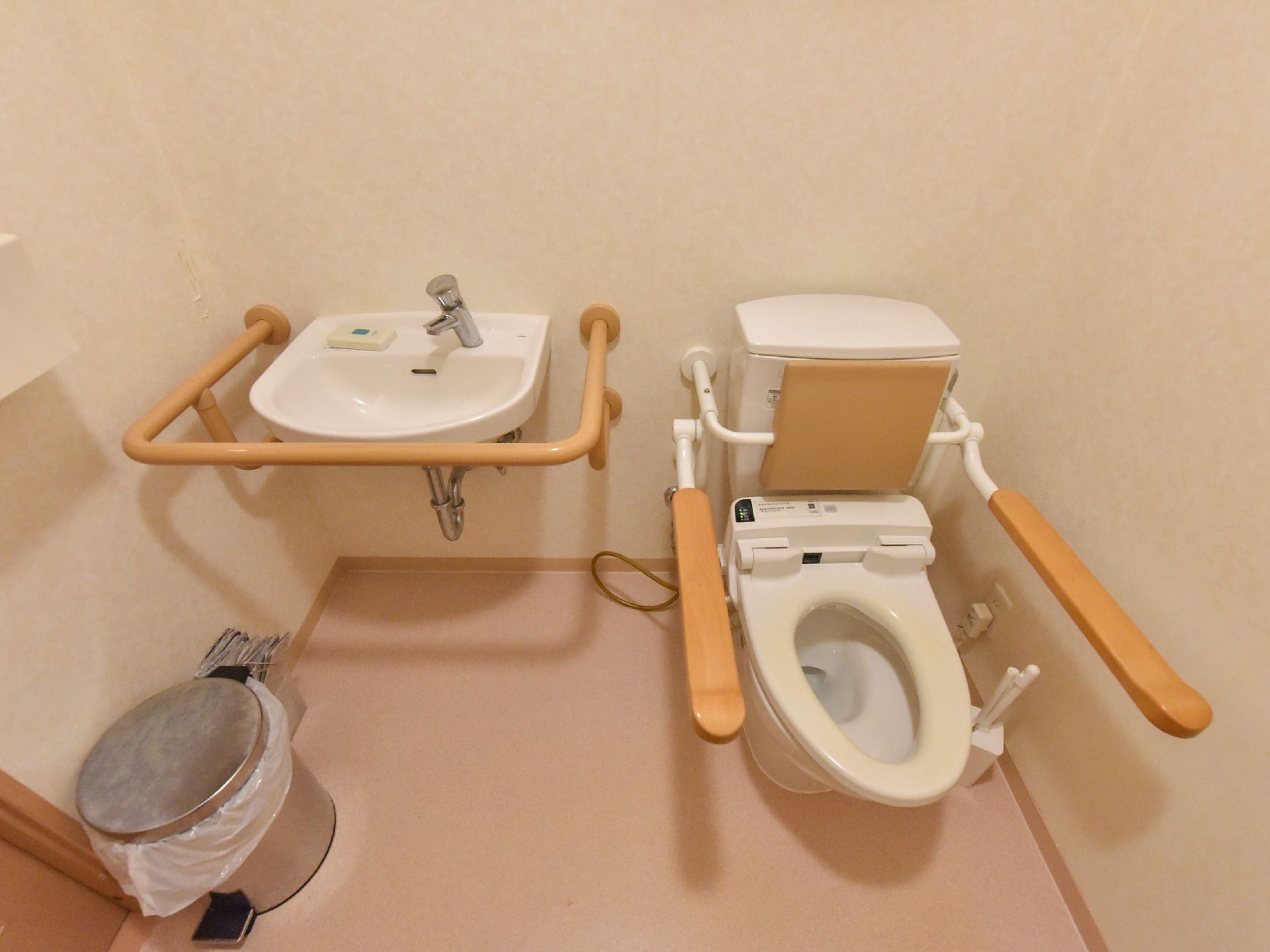 広々としたトイレは、可動式の背もたれや手すりが便器に取り付けられている。手洗い場も独立してあり、手すりも設置されている。