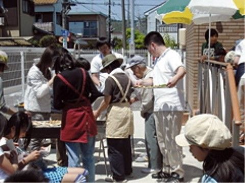 晴れた日に、施設の庭でバーベキューのイベントを楽しんでいる大勢の人々