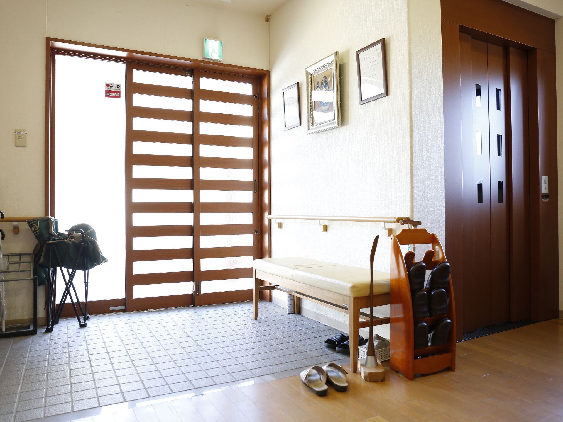 明るく広い玄関である。安全に靴の履き替えが出来るように椅子が置いてある。窓の近くにエレベーターが設置してある。