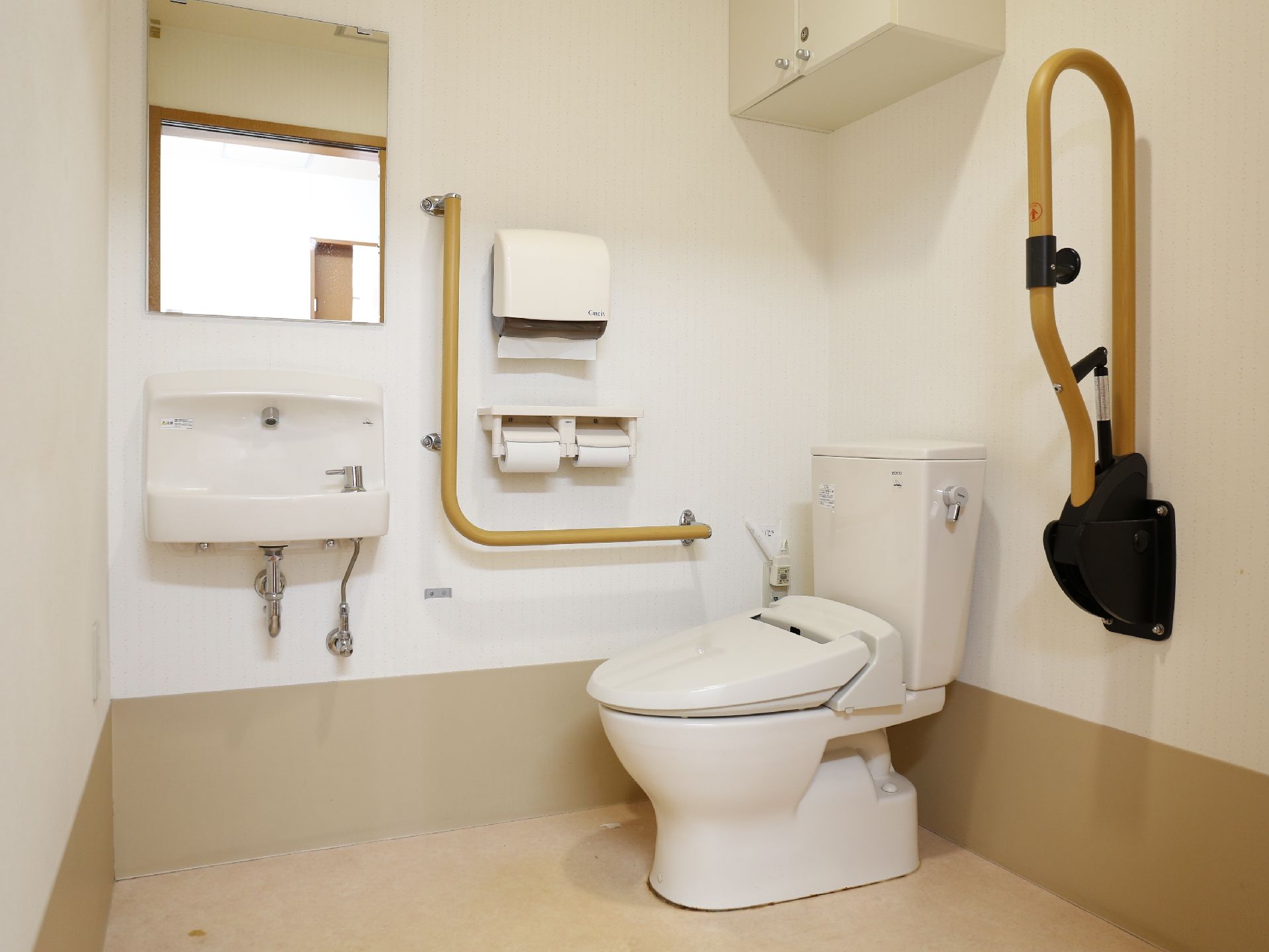 車椅子の方でも入れる広さのトイレである。壁には可動式の手すりが設置してある。手が洗えるよう壁掛け式洗面器も備え付けられている。