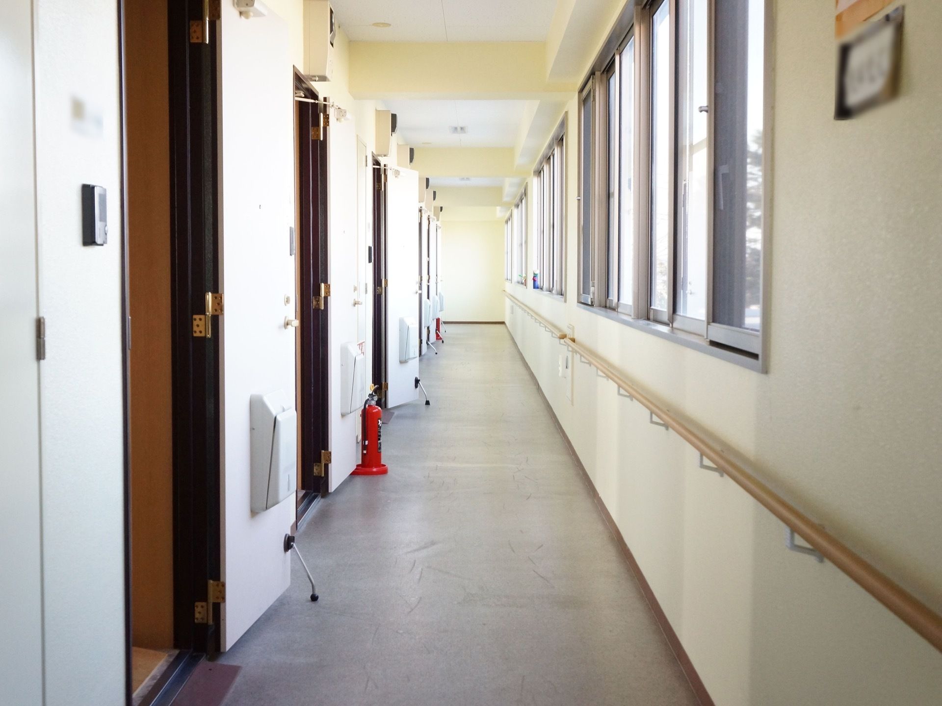 通路の右際には窓が複数ある。その下には長い手すりが取り付けられている。左側には部屋の扉が並んでいて、ストッパーで扉は開放されている。