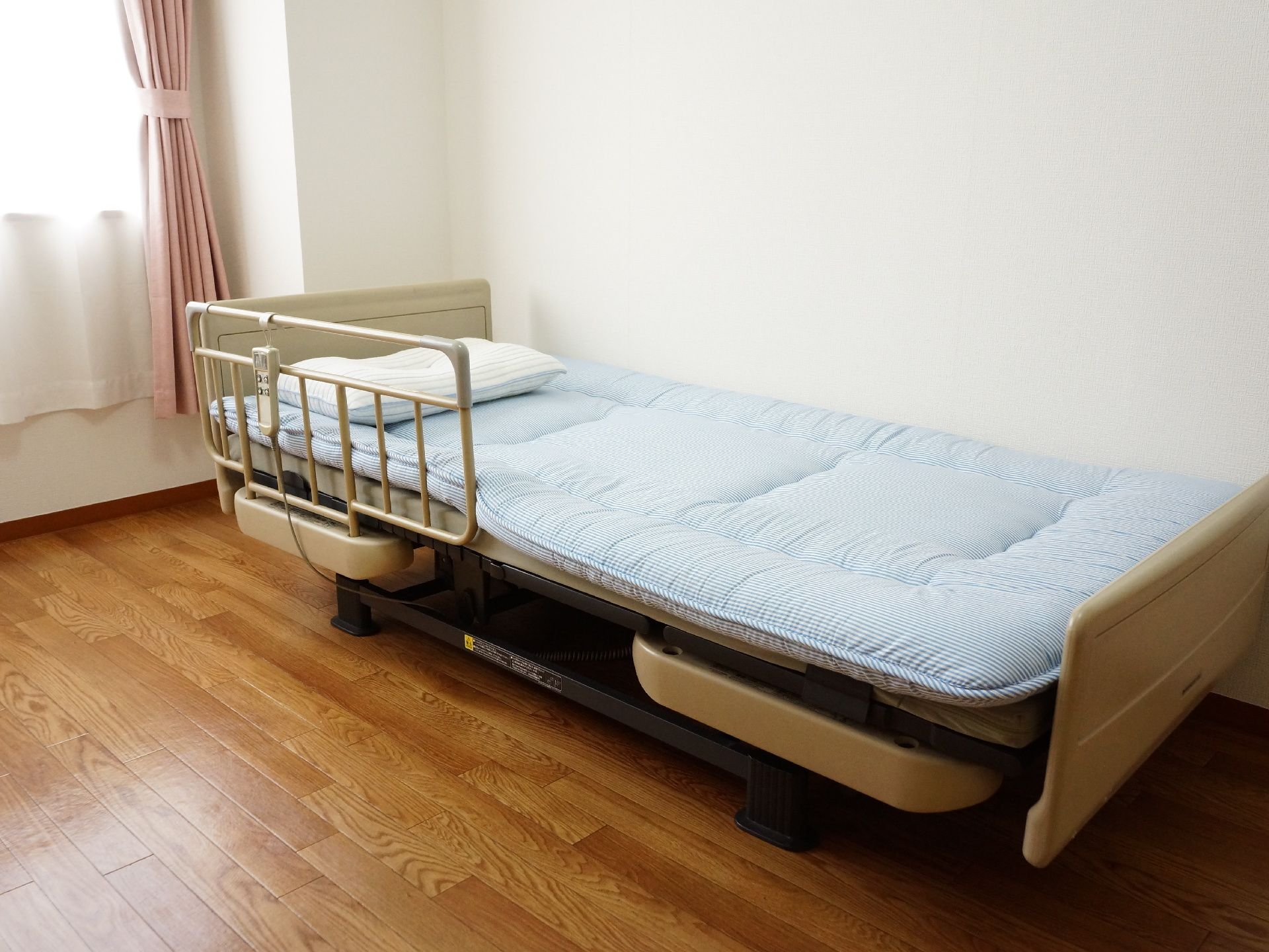 居室の壁際にはベッドが1台置かれている。左側には落下防止用のフェンスがあり、操作用のリモコンが掛けられている。
