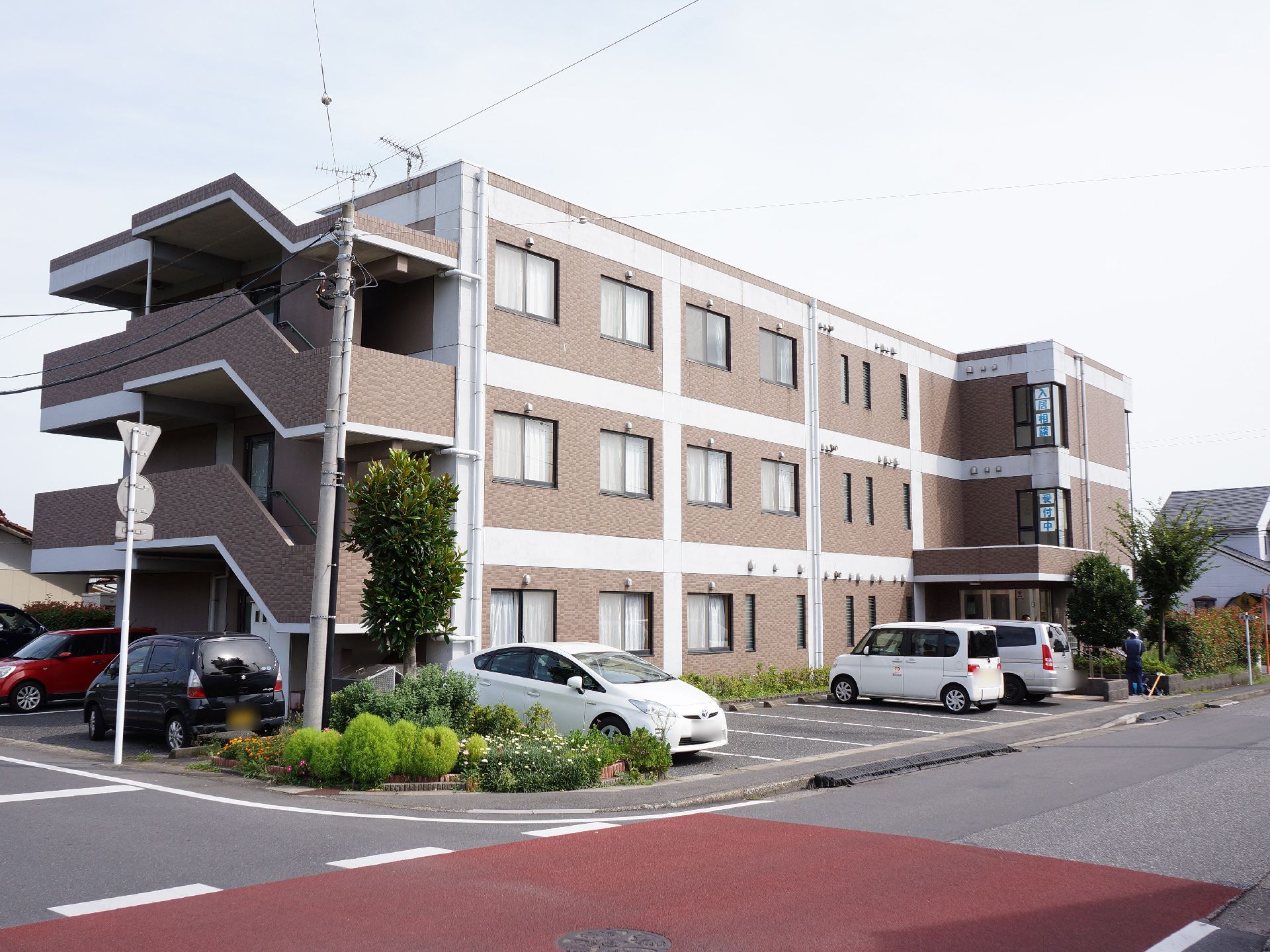 施設は3階建ての建物で、左側には外階段が設置されている。前面と横には駐車スペースが設けられ、各所に植物が植えられている。