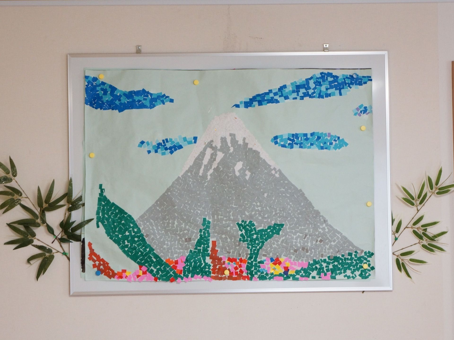 白い壁に大きなちぎり絵が飾ってある。水色の紙にちぎり絵で富士山が描かれており、空には雲が浮かんでいる。