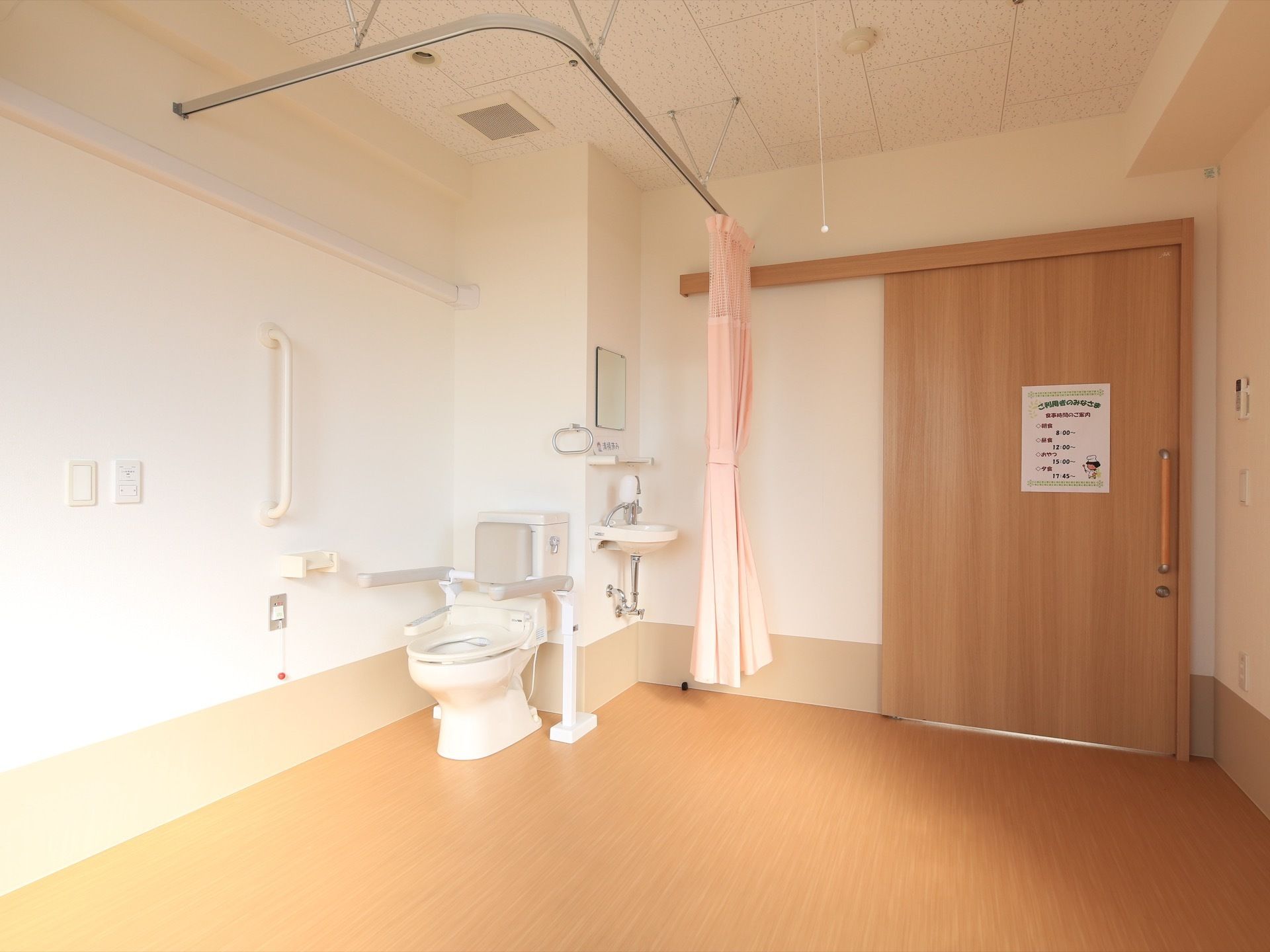 居室入口は大きな取っ手がついた引き戸になっている。壁際にトイレが設置されていて、仕切り用のカーテンがかかっている。