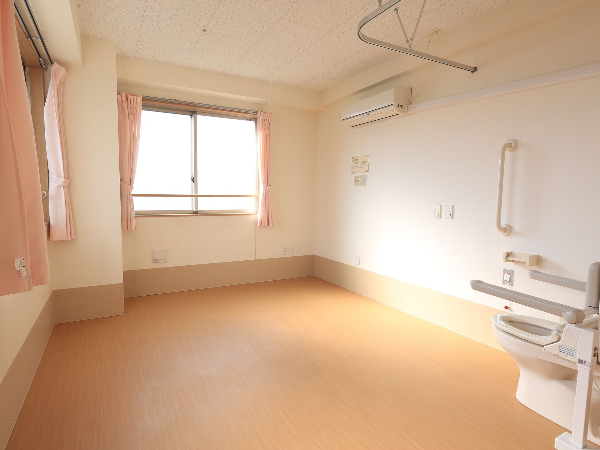 エアコンが完備されたフローリングの床の日当たりの良い洋室で、トイレとはカーテンで仕切られるようになっている。