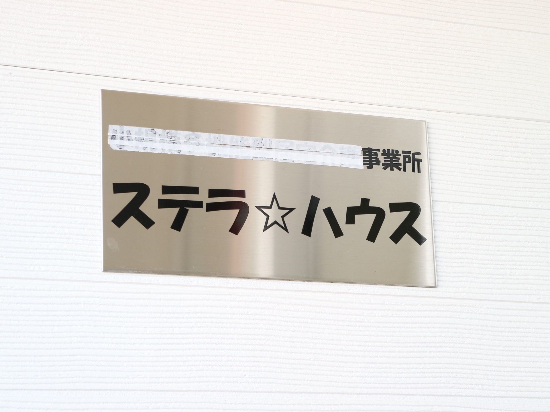凹凸のある白を基調とした外壁に、表札が取り付けられている。ステンレスのパネルに、施設名が書かれている。