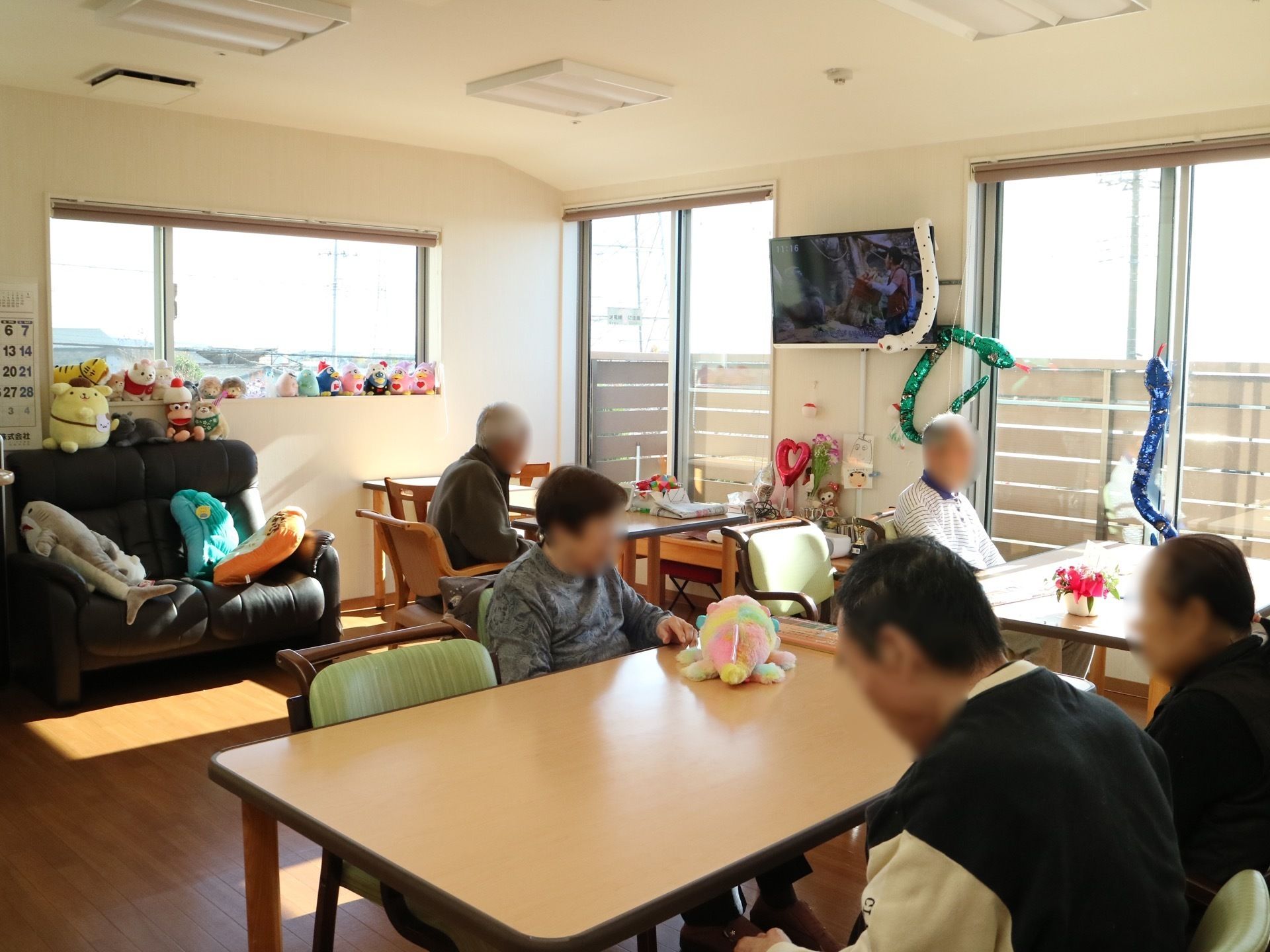 外光が差し込む明るい食堂で、壁や窓に蛇の装飾が施されている。椅子に座って、入居者様が思い思いの時間を過ごしている。