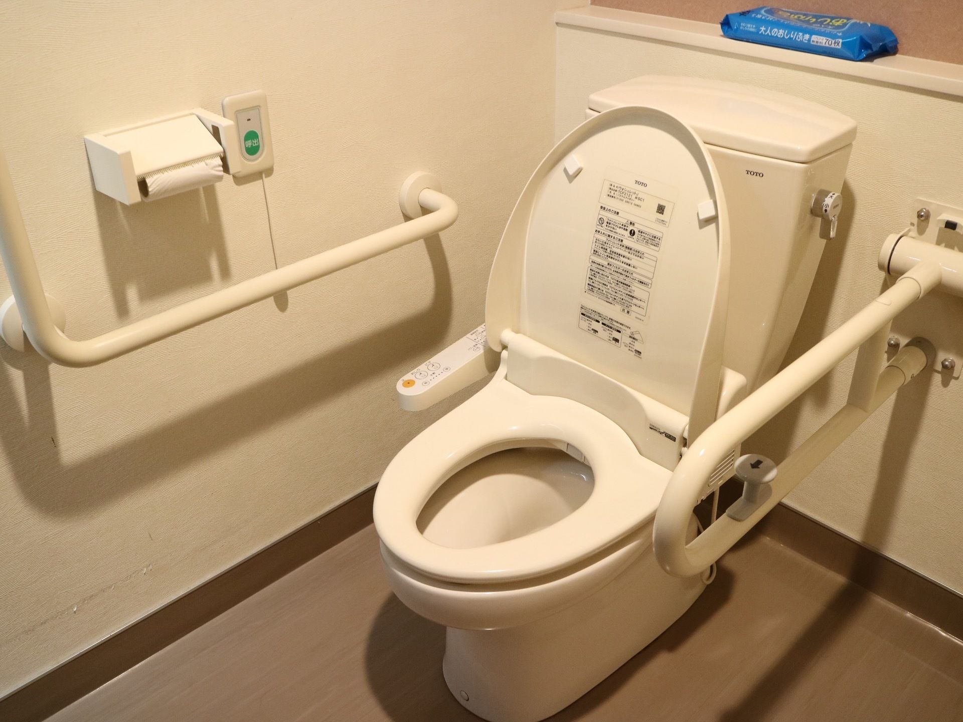 白を基調とした個室トイレで、温水洗浄機能付きの便座が採用されている。便器の両サイドには、手すりが設置されている。