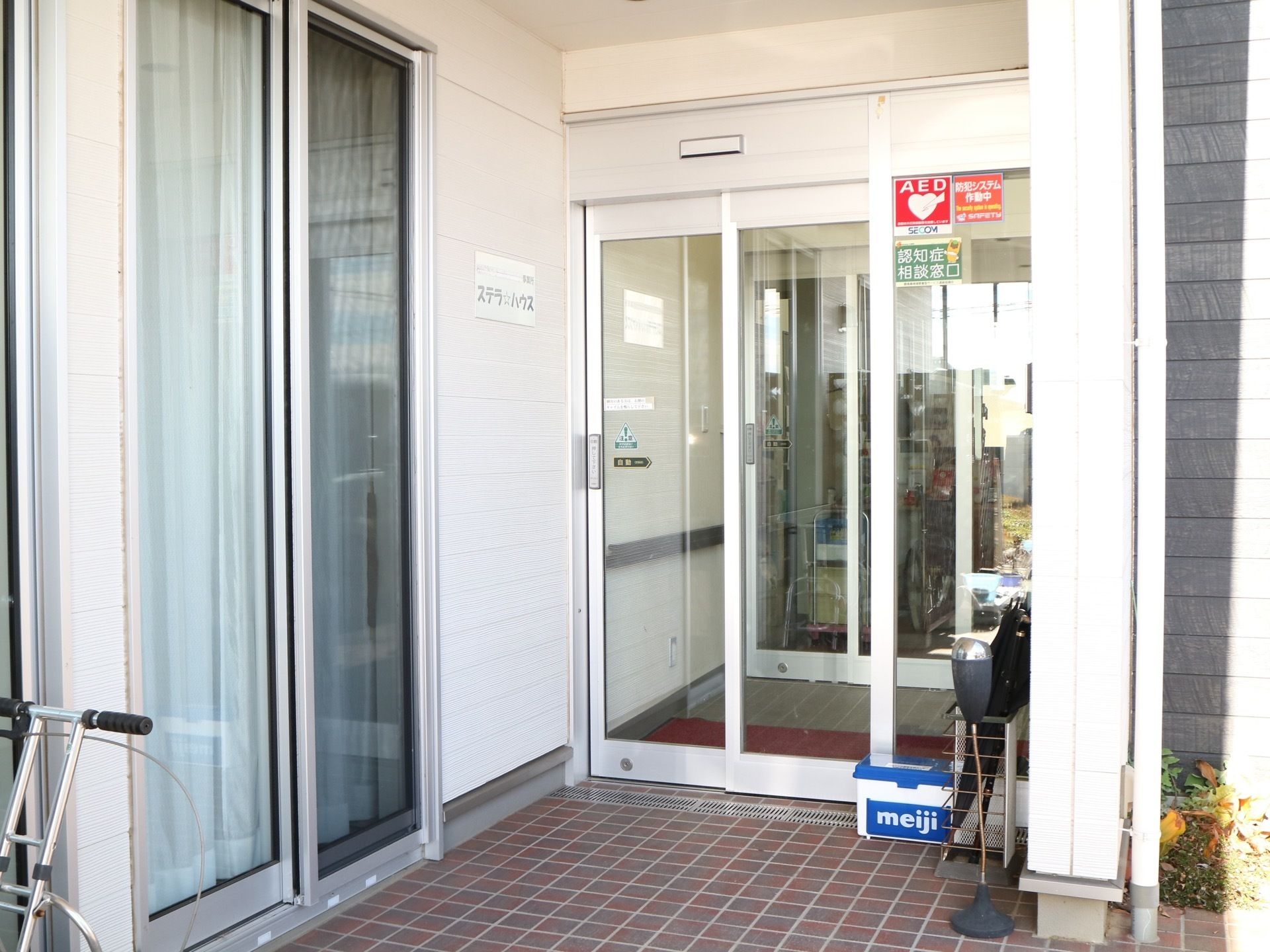 ガラス戸の自動ドアが採用された玄関で、床はタイル張りとなっている。横の外壁には、表札が設置されている。