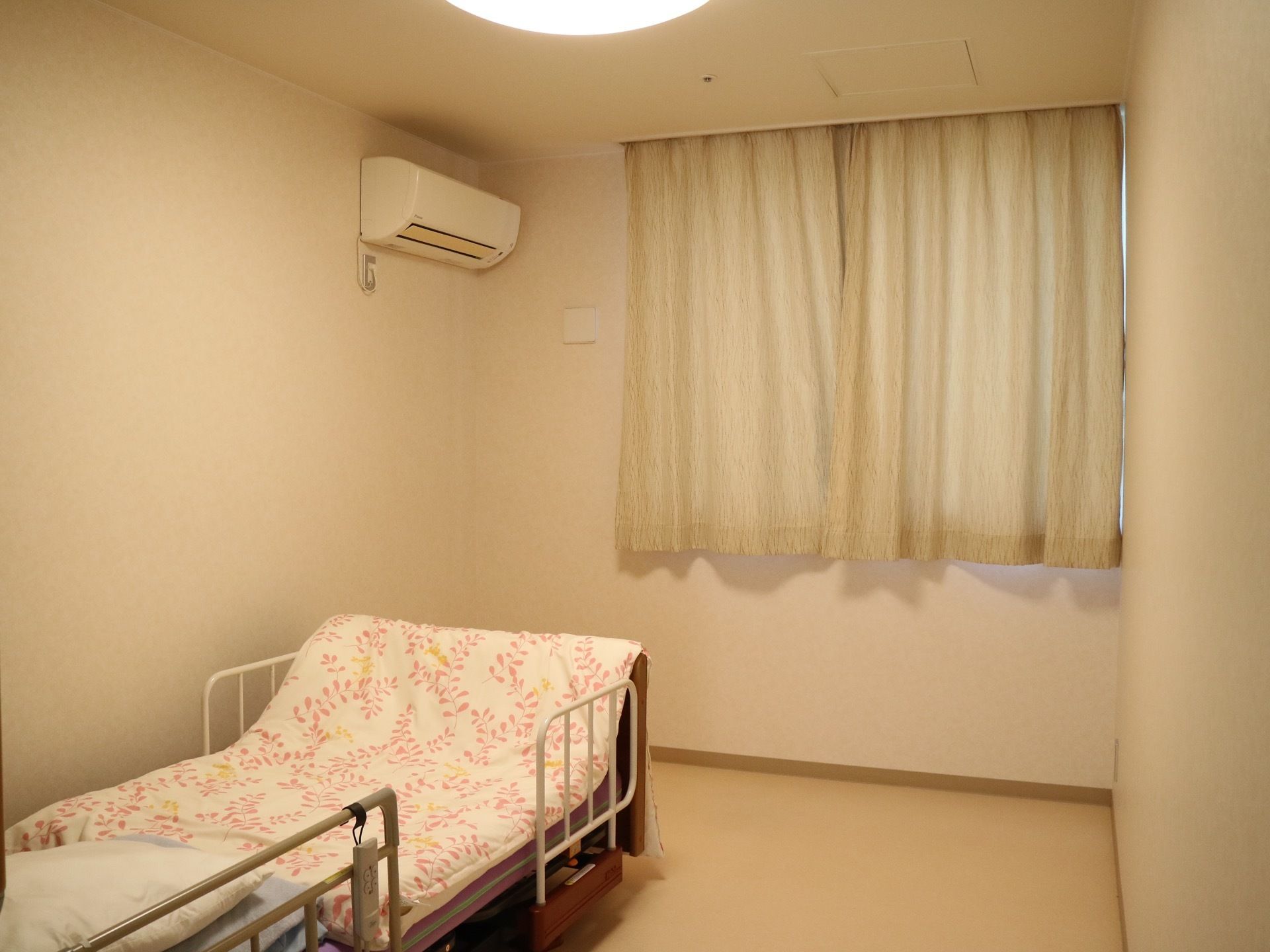 エアコンが完備されている居室で、室内にはリモコンで操作可能なリクライニングベッドが置かれている。窓にはカーテンが取り付けられている。