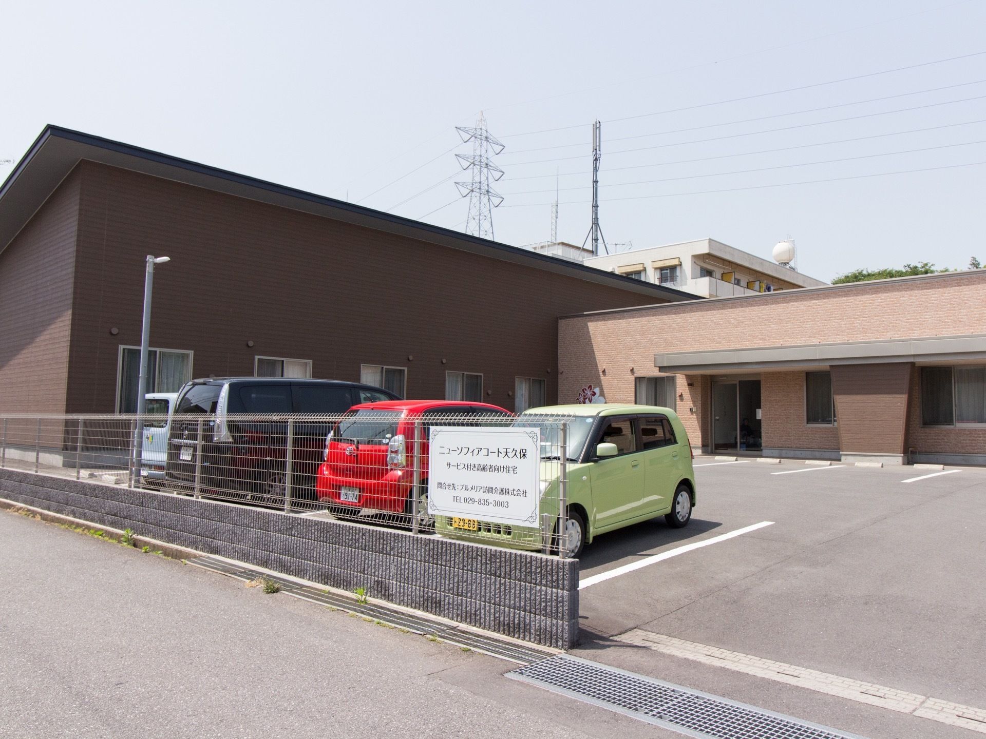 施設は茶色を基調とした１階建ての建物である。施設前には駐車場が設けられており、数台の車が停まっている。