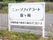 中央に白色の看板が立っており、そこには施設名や住所が書かれている。看板の後側には白い柵が立っている。