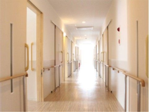 廊下の両サイドには、白くて大きな引戸の取りつけられた居室が並んでいる。茶色い手すりも腰の高さに設置されている。