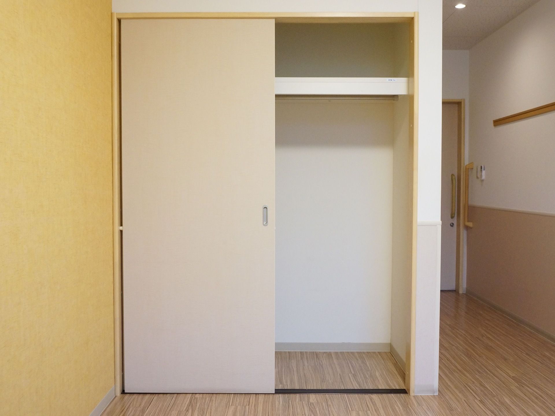 居室の収納の扉を開けた写真。上部には棚があり、その下には洋服をハンガーでかけられる長いバーが設置されている。